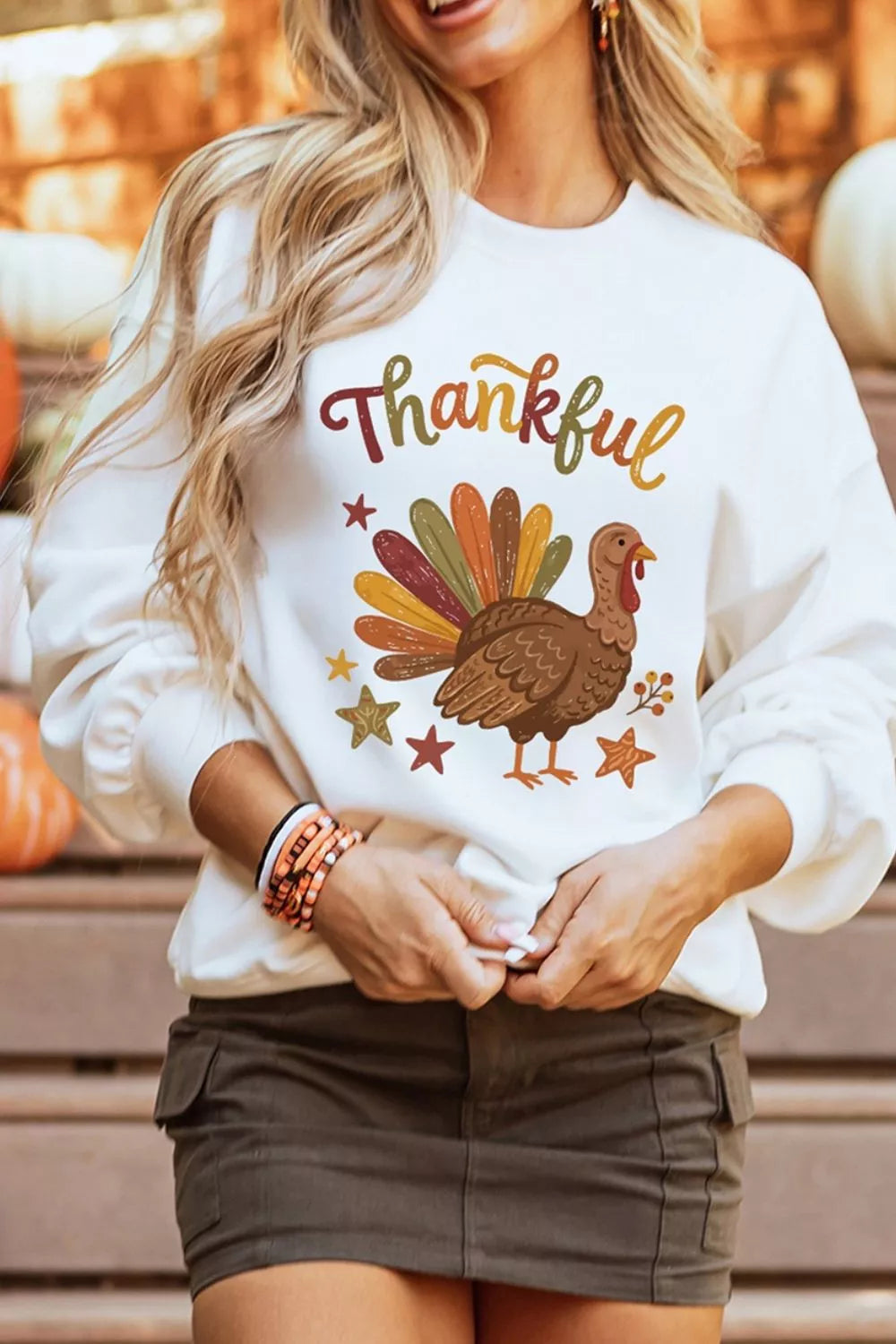 Blonde Model hält Saum des herbstlichen Sweatshirts mit Truthahndruck bei unscharfen Kürbissen im Freien