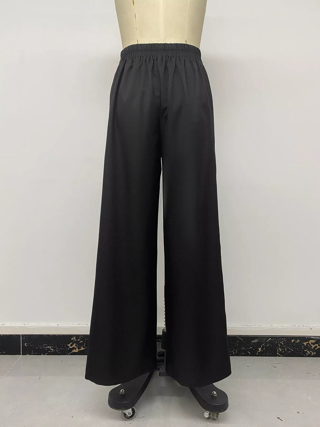 Rear view of black wide-leg pants on mannequin emphasizing loose flowing floor-length cut