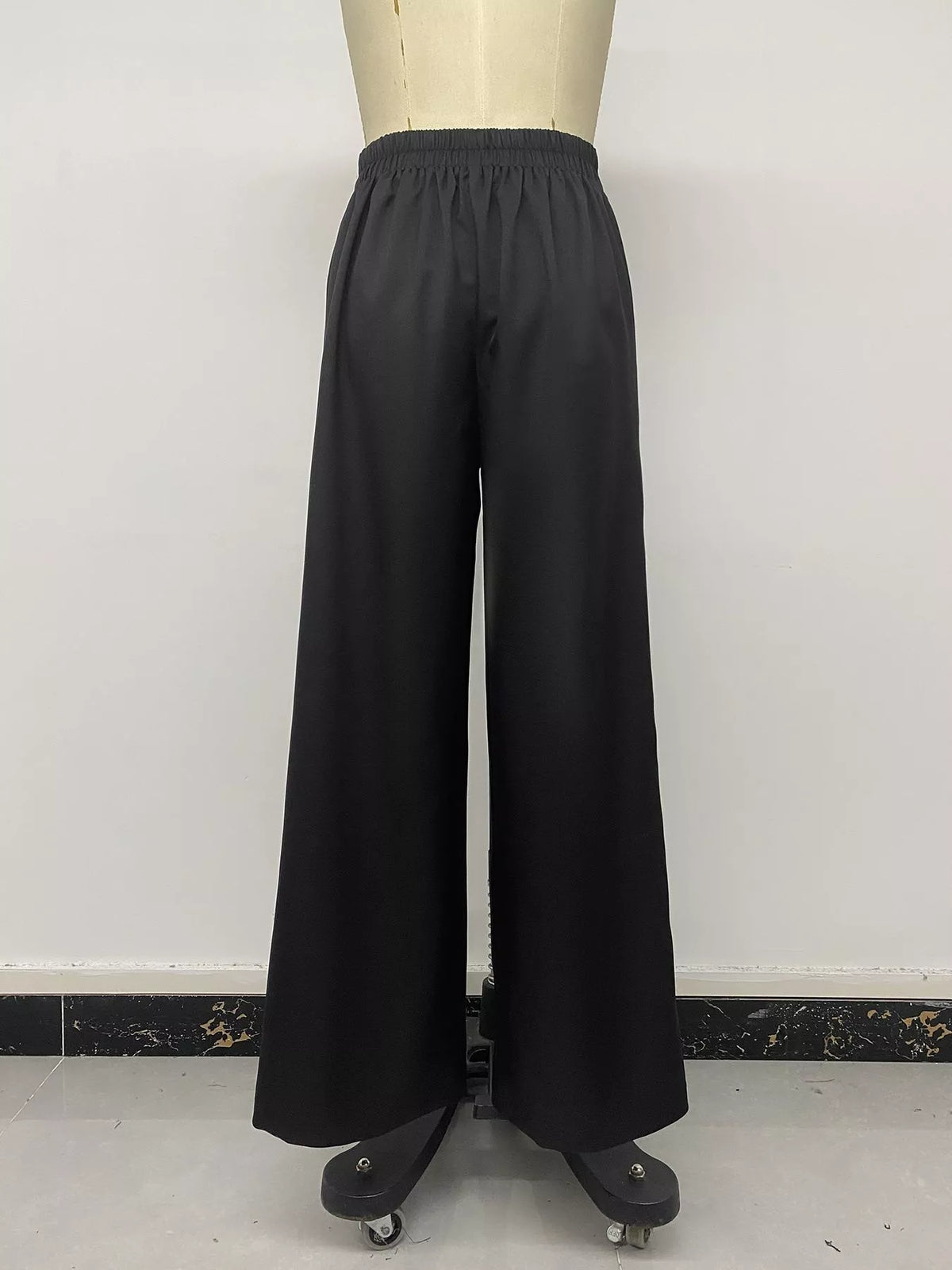 Rear view of black wide-leg pants on mannequin emphasizing loose flowing floor-length cut