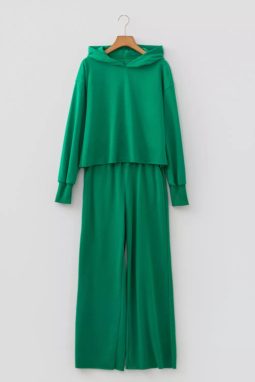 Conjunto de dos piezas verde colgado en percha sobre pared blanca: sudadera corta y pantalón amplio para descanso diario.