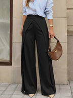 Model wearing black high-rise trousers with asymmetrical waist against beige background