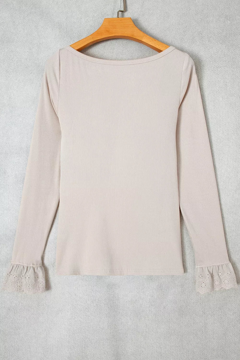 Light beige top hanging on wooden hanger showing ribbed knit and lace details