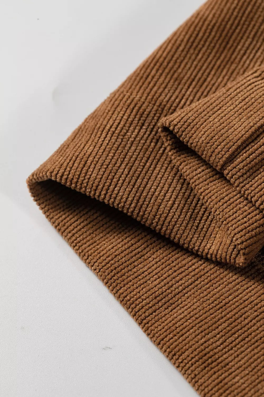 Detalle del dobladillo plegado de pantalones de pana camel, mostrando textura acanalada consistente y acabado de borde limpio
