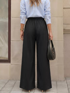 Back view of black wide-leg trousers revealing elasticated gathered waistband design