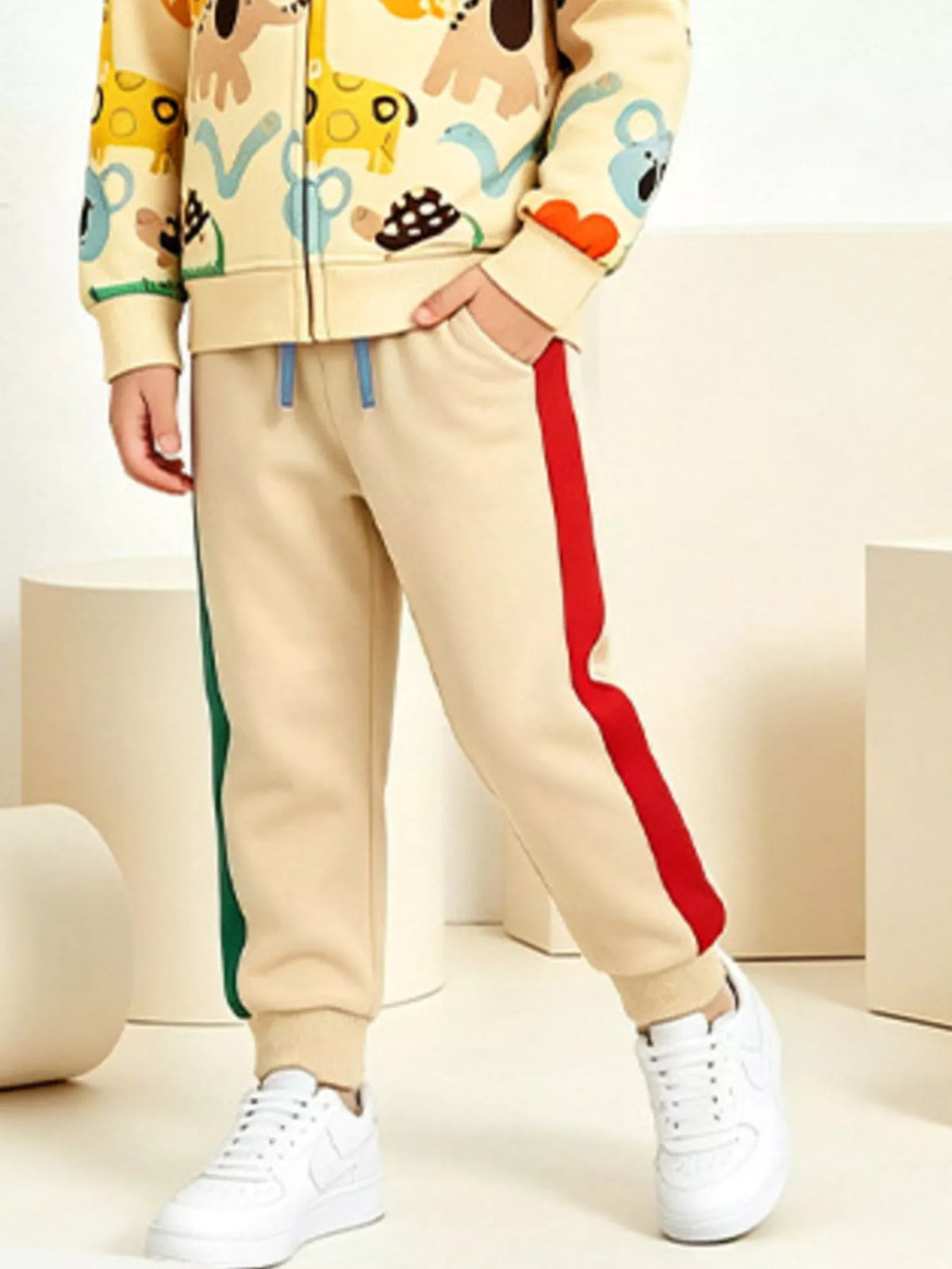 Beige Jogginghose mit roten und grünen Seitenstreifen, elastische Bündchen und Hand in der Tasche