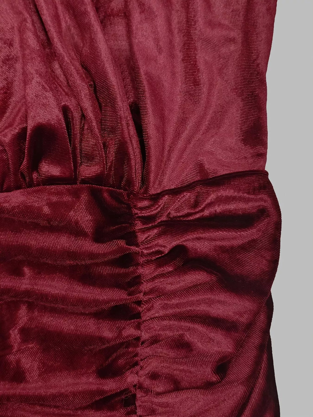 Détail du tissu velours bordeaux foncé avec fronces verticales créant un effet texturé sur fond gris