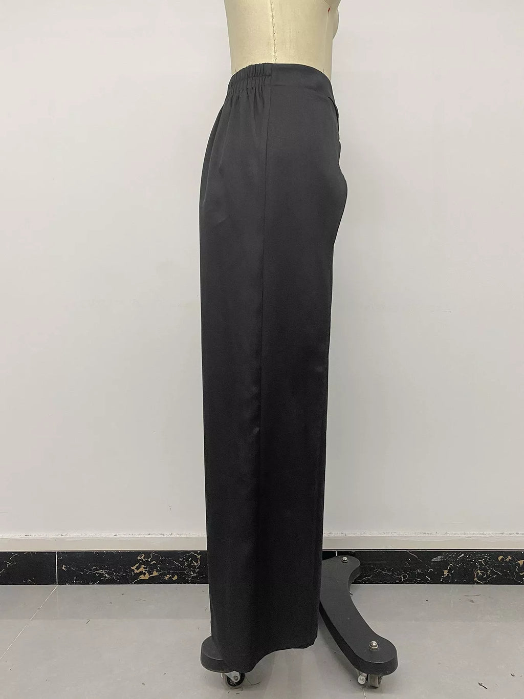 Side profile of black trousers on mannequin showing smooth vertical drape to hem