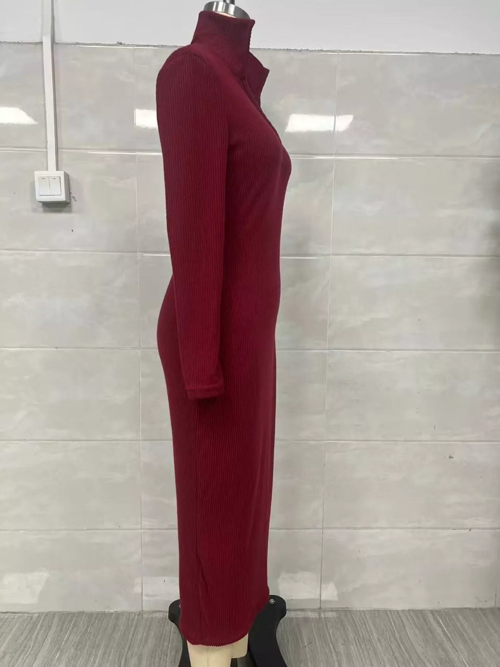 Profil latéral d'une robe tricotée côtelée bordeaux sur mannequin illustrant le tissu épousant le buste et la coupe midi ajustée globale