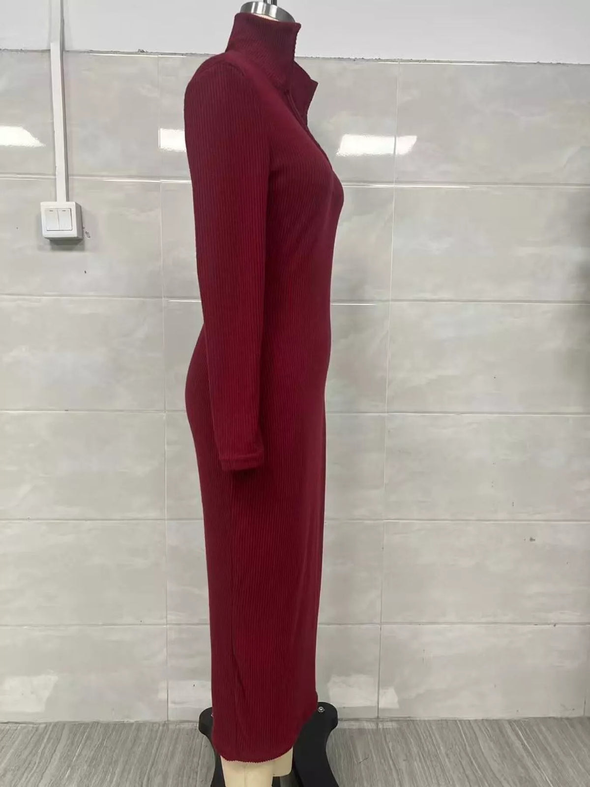 Profil latéral d'une robe tricotée côtelée bordeaux sur mannequin illustrant le tissu épousant le buste et la coupe midi ajustée globale