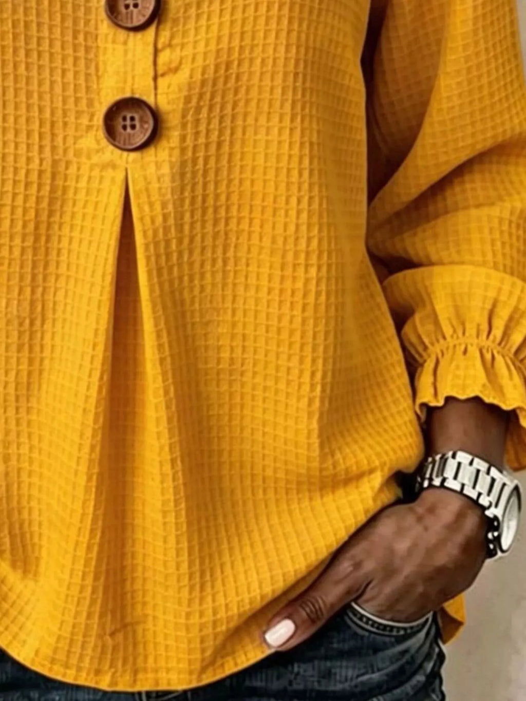 Torso inferior de la blusa amarilla mostrando caída del tejido y puño recogido