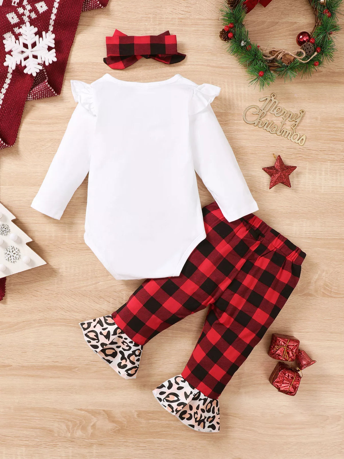 Disposición plana completa del conjunto navideño de tres piezas para niña con body, pantalones a cuadros, diadema y guirnalda festiva